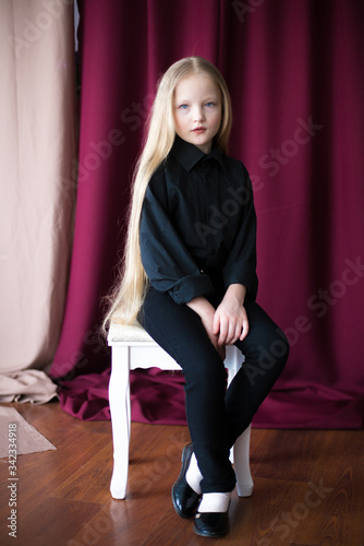 Cute little girl with long blond hair in a black shirt and jeans on a red background in the studio