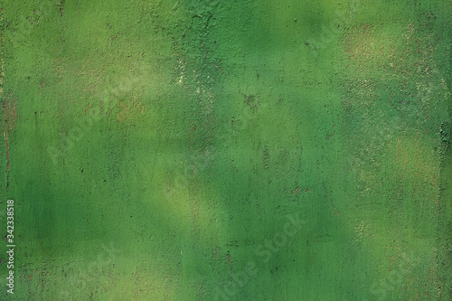 Green painted surface of a metal gate closeup. Texture with a gradient of green on the metal surface. Old painted peeling house wall background.