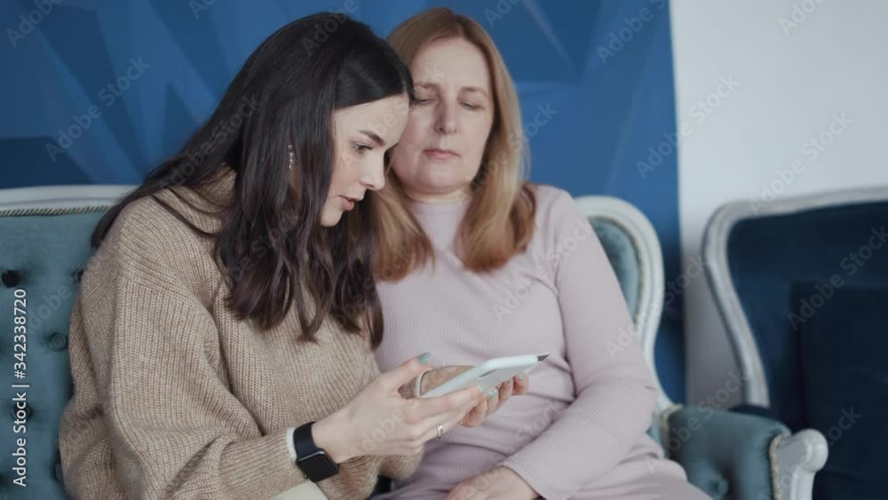 Online shopping from home. The adult daughter explains to her mother how to make purchases remotely using a bank card and smartphone. Online shopping from home. The adult daughter explains to her mother how to make purchases remotely using a bank card and smartphone.
