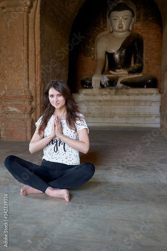 An adorable girl is meditating in lotus position, sitting on the floor in front of a Buddha statue in an ancient temple in Bagan in Myanmar.