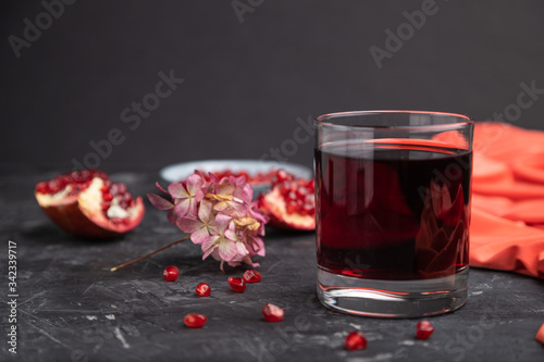 Glass of pomegranate juice on a black concrete background. Side view, copy space.