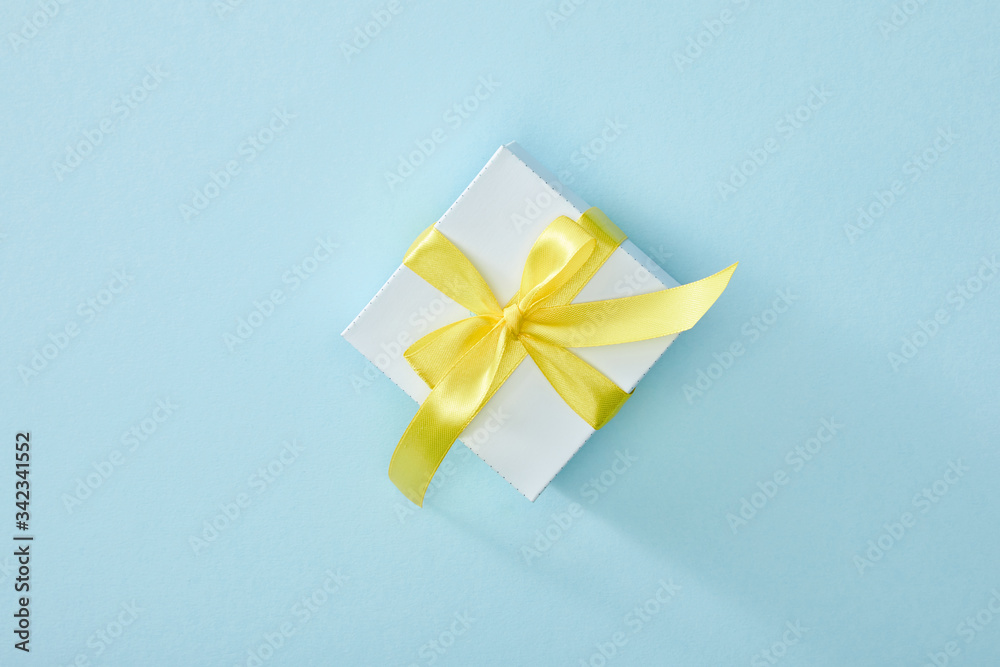 top view of festive gift box with yellow ribbon on blue background top view of festive gift box with yellow ribbon on blue background