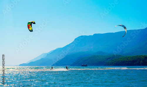 Fototapeta Naklejka Na Ścianę i Meble -  Akyaka, Mugla/Turkey-August 14 2018: Two surfers enjoying kite surfing at the beach where Azmak River meets the Mediterranean Sea