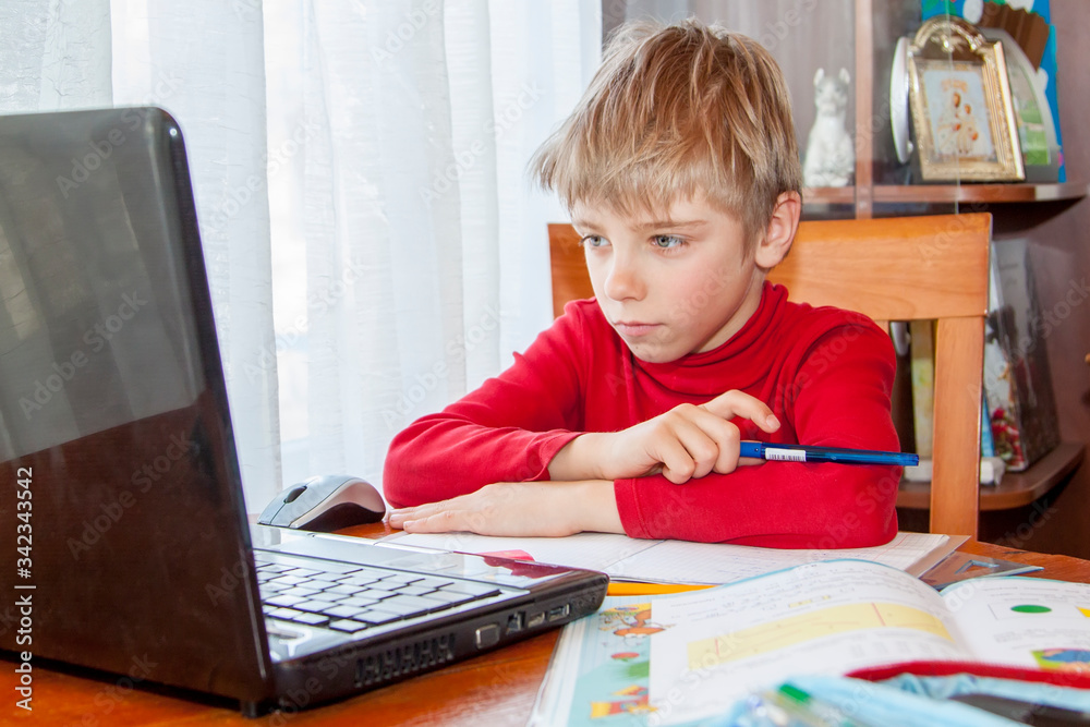 School kid in self isolation using laptop for homework, Social Distance learning online education during coronavirus epidemic. Cute boy studies and does school homework at home during quarantine School kid in self isolation using laptop for homework, Social Distance learning online education during coronavirus epidemic. Cute boy studies and does school homework at home during quarantine
