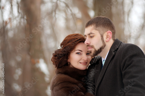 A beautiful brown-haired woman leaned against the shoulder of her man with a beard and smiles in a winter park close-up.