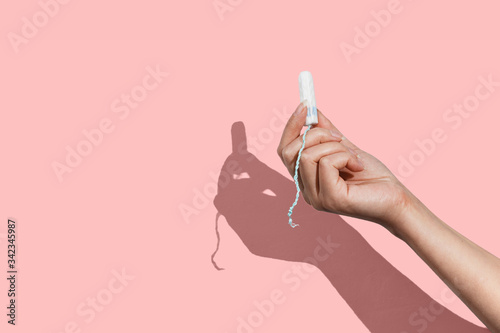 Woman's hand holding a clean cotton tampon on the pink background. Direct light. photo