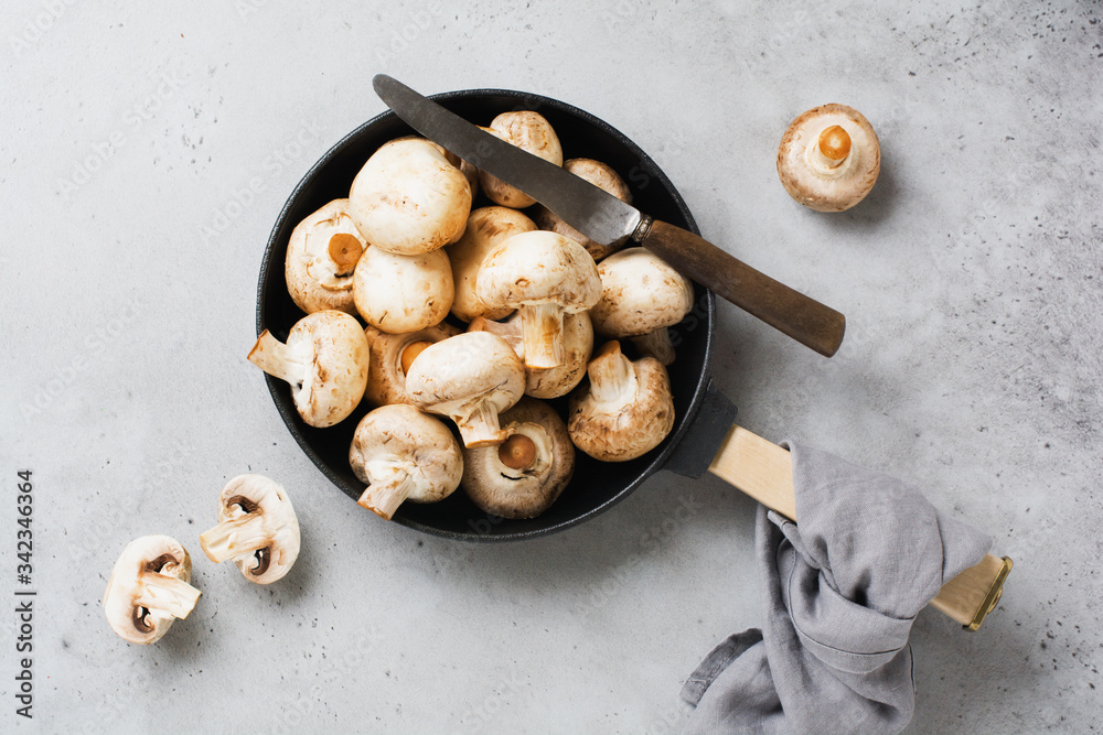 Raw Champignon mushrooms in a cast-iron old pan on an old concrete gray rustic background for frying. Top view. Raw Champignon mushrooms in a cast-iron old pan on an old concrete gray rustic background for frying. Top view.