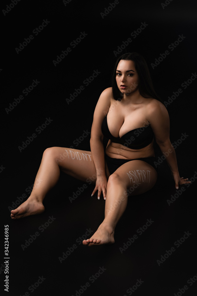 Plus size model in underwear with lettering I Did not Ask For It on body sitting isolated on black