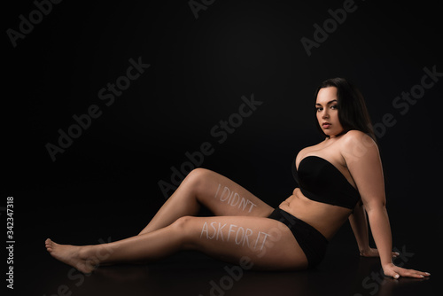 Side view of plus size model with lettering I Did not Ask For It on body on black background © LIGHTFIELD STUDIOS