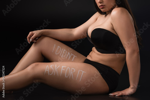 Cropped view of plus size model with lettering I Did not Ask For It on body on black background