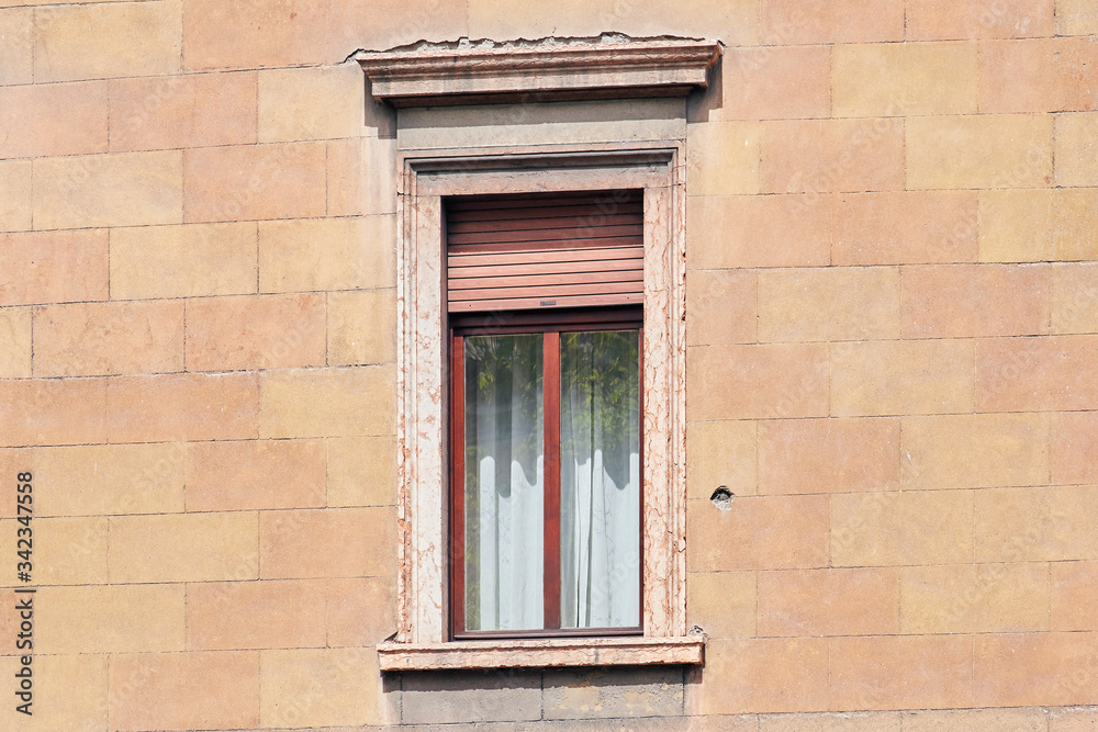 Fototapeta premium Italian window on the sandy-yellow bricked wall facade with open brown color roller shutters