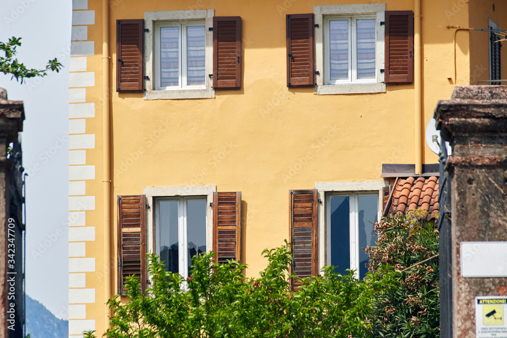 Italian windows on the yellow wall facade with open brown color classic shutters