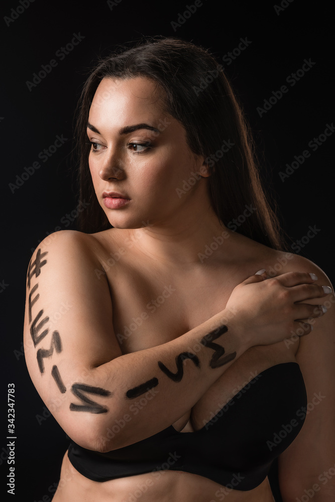 Portrait of plus size model in black bra with lettering hashtag feminism on body isolated on black Portrait of plus size model in black bra with lettering hashtag feminism on body isolated on black