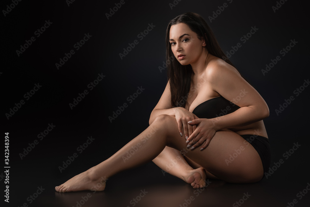 Fototapeta premium Side view of attractive plus size girl touching her leg on black background