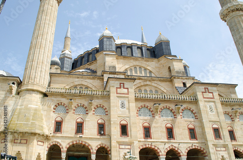 Sunny, clear blue sky. Minarets of light yellow limestone, marble, dark blue, gray domes on roof of mosque. Bright juicy fresh green leaves on trees. Copy space. Selective focus Turkey, Edirne