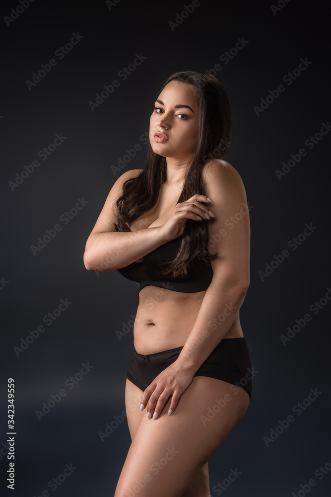 Plus size girl in underwear covering body with hands on black background Plus size girl in underwear covering body with hands on black background