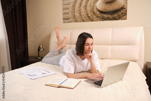 Young  woman businessman on self-isolation during a coronovirus pandemic COVID-19 on self-isolation works at home, lying on bed, checks mail, does his work remotely, telework