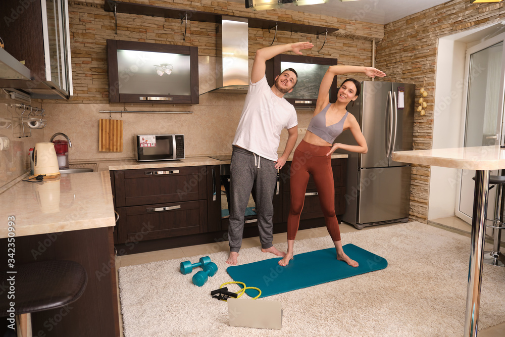 Obraz premium Athletic man and woman blogger in sportswear doing sports exercises at home in the kitchen together. Stay at home activities. Prevent infection from the pandemia.