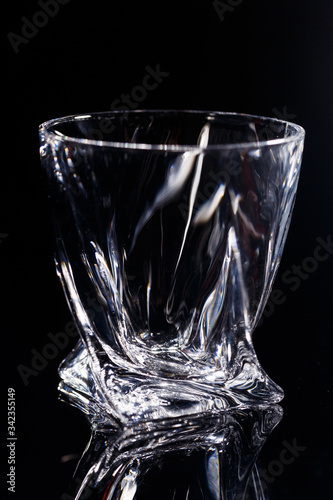 Black background stands a clean glass with reflection on a glass table. Facets on a Glass Cup