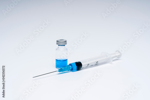 Syringe with vaccine in a vial bottle with blue liquid on white background.