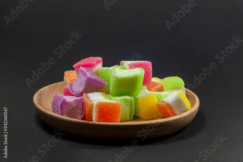 Multi colored jelly in a wooden tray against a black patterned background