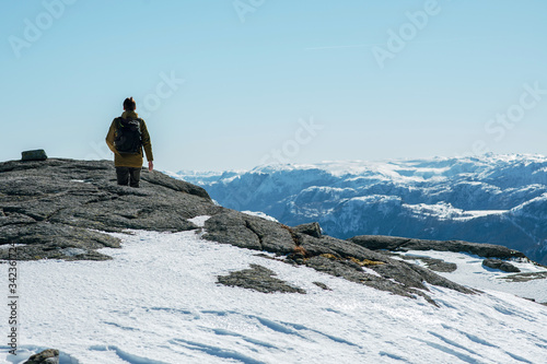 Rear view of a traveler man walking along the rocks. Beautiful snowy mountain landscape near the Pulpit Rock, Preikestolen, Lysefjord, Norway. © WellStock