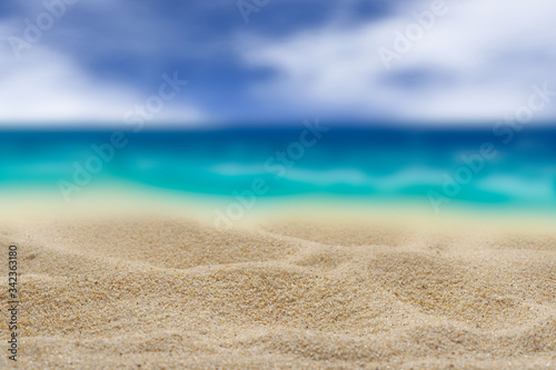 Background. Clean sand on a background of the blurry turquoise sea. Cloudy sky.