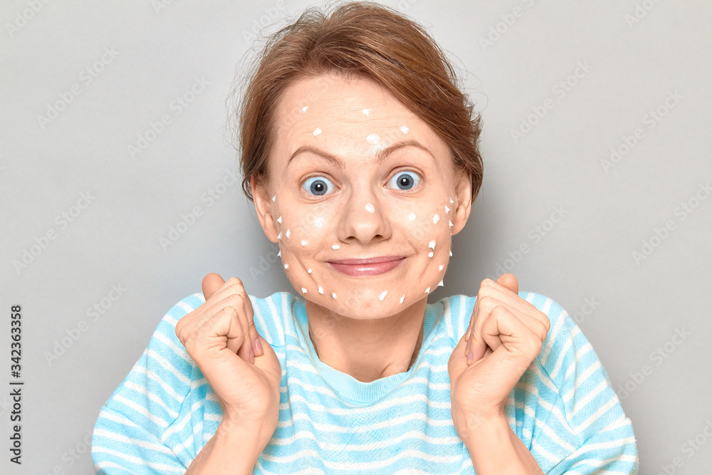 Portrait of overjoyed girl with white drops of face cream on skin