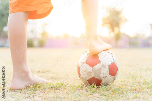 Fototapeta Naklejka Na Ścianę i Meble -  The legs of a little boy with an old red and white football in the morning.