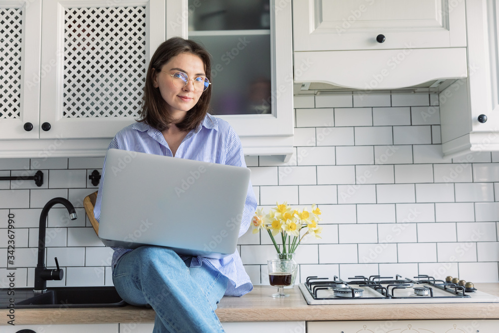 Attractive young woman using laptop and sitting in the kitchen. Businesswoman, work from home, distance education, online learning Attractive young woman using laptop and sitting in the kitchen. Businesswoman, work from home, distance education, online learning