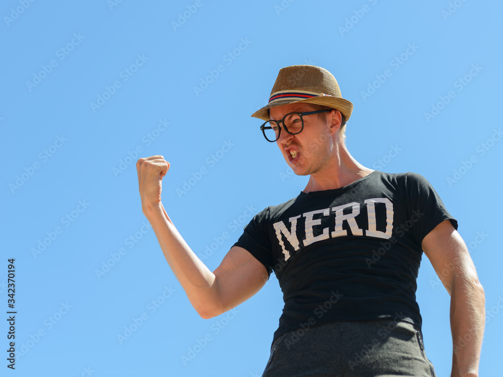 Young nerd tourist man with fist raised against blue sky