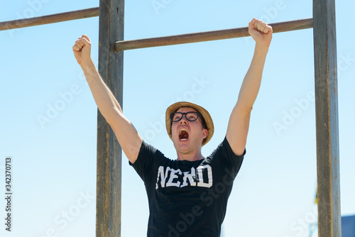 Young nerd tourist man getting good news against blue sky