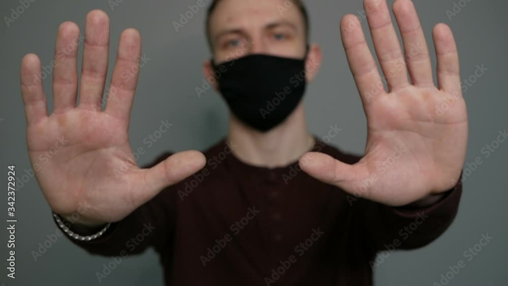 Young guy in a protective mask on a gray background. Shows hands. Hygiene Young guy in a protective mask on a gray background. Shows hands. Hygiene