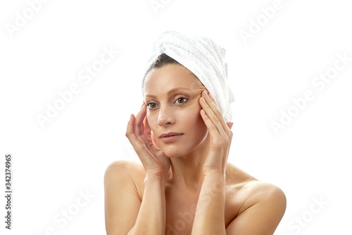 Beautiful young woman with a white towel on her head and with clean perfect skin does facial massage at home. Massage the skin around the eyes. Isolated white background.