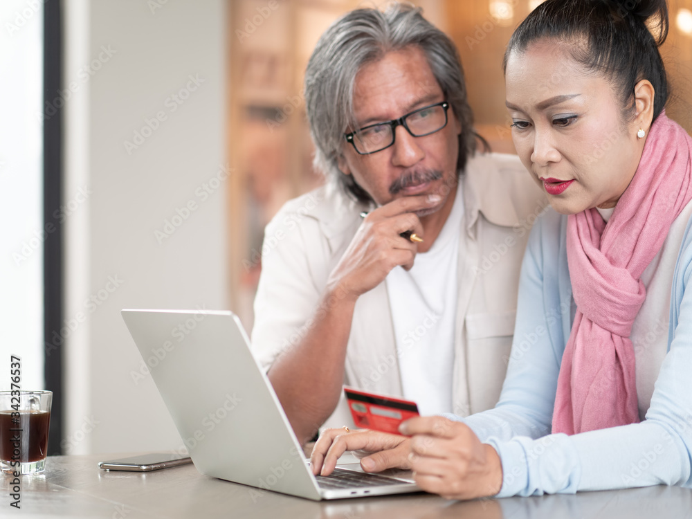Asian senior couple using a credit card and laptop while working on their finances at home. Technology, Finance and communication Asian senior couple using a credit card and laptop while working on their finances at home. Technology, Finance and communication