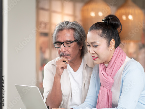 Asian senior couple using laptop sitting in room work from home. Technology and communication