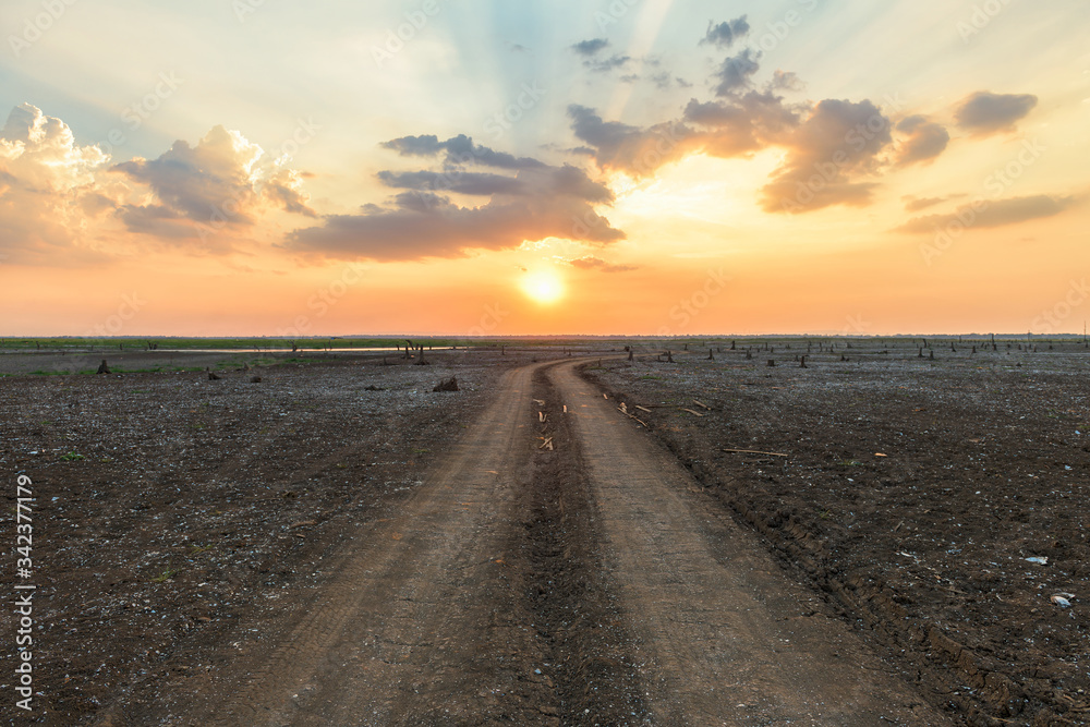 Dirt road in the parched lake with sunset sky