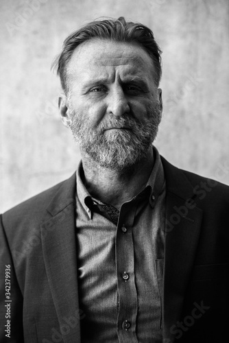 Mature handsome bearded businessman wearing suit in black and white
