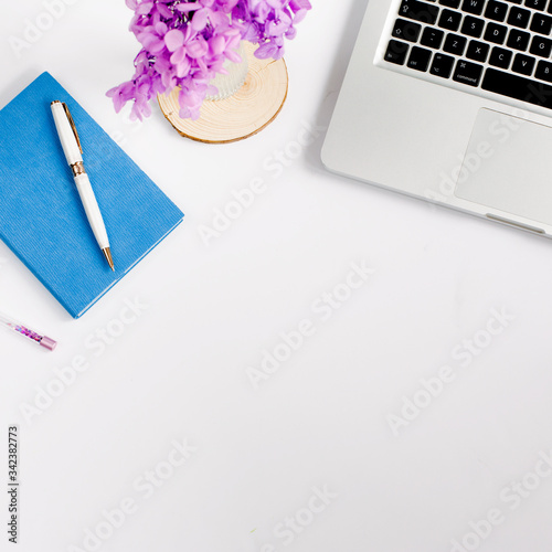 Bright and colorful children desktop with blue notebook, laptop, pink gift and purple flowers. Flat lay homework concept