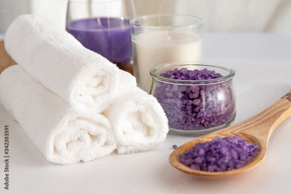 Home beauty essentials & spa concept.  Self-care in quarantine & self-isolation.  White towels folded into a roller on a white background, white and lilac candle, salt for scrub smell color  lavender.