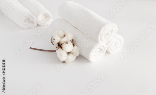 Home beauty essentials concept. Self-care in quarantine and self-isolation. Spa and cleanliness concept. On a white background folded in a roller white towels, a branch with cotton flowers.