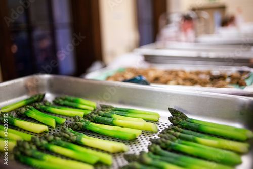 Freshly boiled asparagus spears placed on a stainless steel tray ready to be used in a seaasonal dish photo