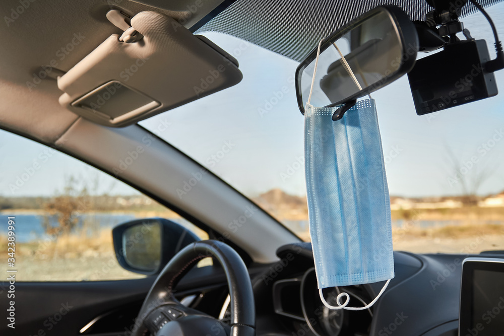 Blue medical protective face mask is hanging on the rearview mirror. Concept of protection from bacteria and viruses. Closeup Blue medical protective face mask is hanging on the rearview mirror. Concept of protection from bacteria and viruses. Closeup