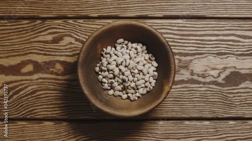 Dried white beans fill a wooden dish. Top view, stop motion.