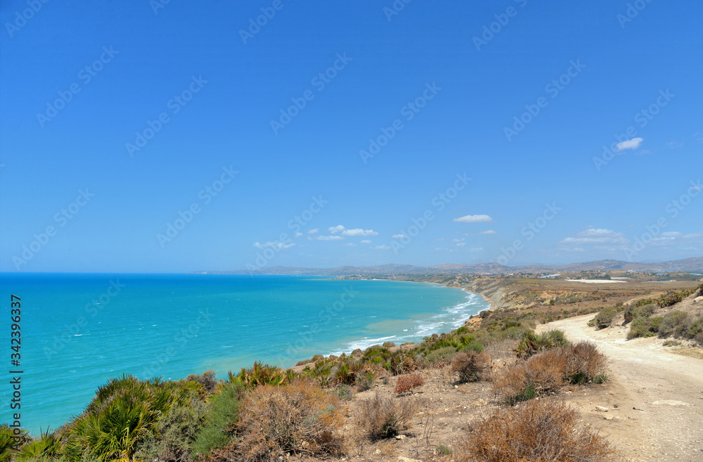 deserted dirt road on a promontory towards the sea and lonely beach in summer day