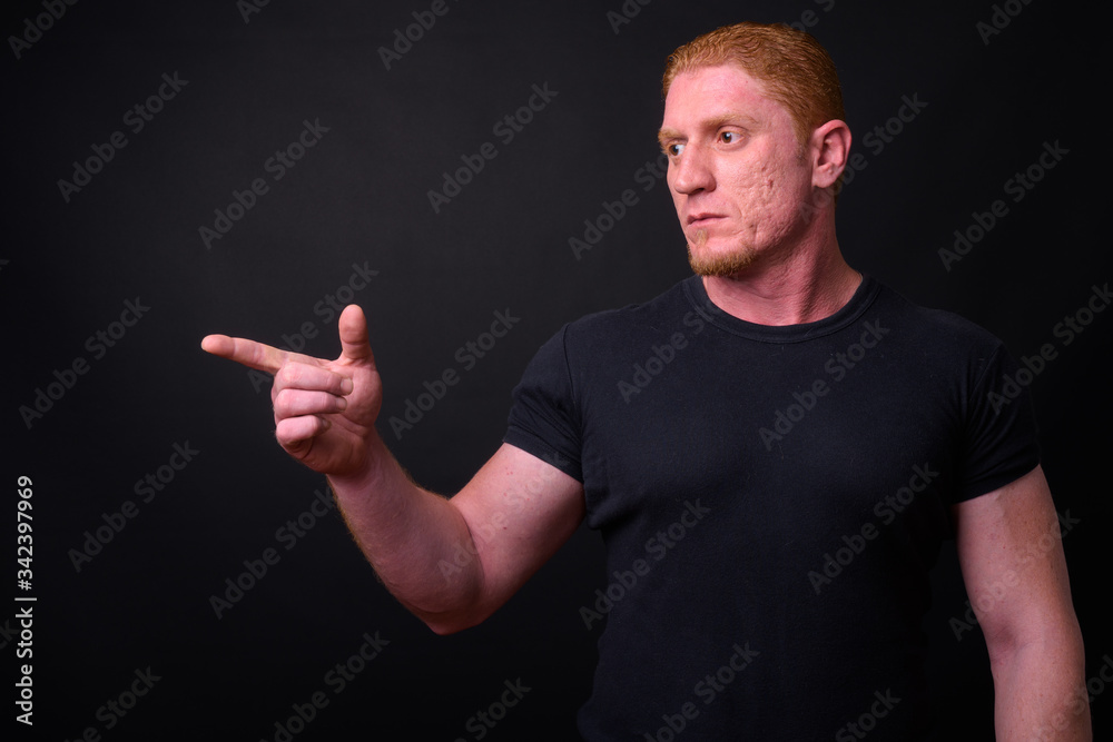 Portrait of muscular man with orange hair thinking and pointing finger Portrait of muscular man with orange hair thinking and pointing finger