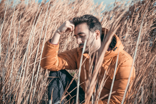 Caucasian man sitting in a field. yellow quilted coat. sunny day