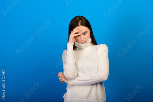 Portrait of a girl in a medical mask, which puts on a rubber glove. Blue background. Copy space. © Ivan Zelenin