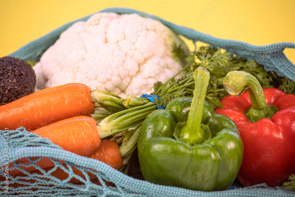 Close up off colorful fresh vegetables in a mesh bag, reusable, sustainable, eco friendly, plastic, zero waste concept. Various vegetables, on yellow background, healthy eating concept. Close up off colorful fresh vegetables in a mesh bag, reusable, sustainable, eco friendly, plastic, zero waste concept. Various vegetables, on yellow background, healthy eating concept.