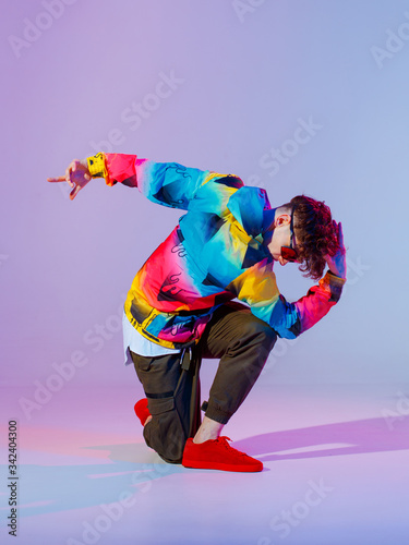 Guy dancing contemporary dance in studio. Neon light grey background. Acrobatic bboy dancer. Break dance lessons. © Georgii